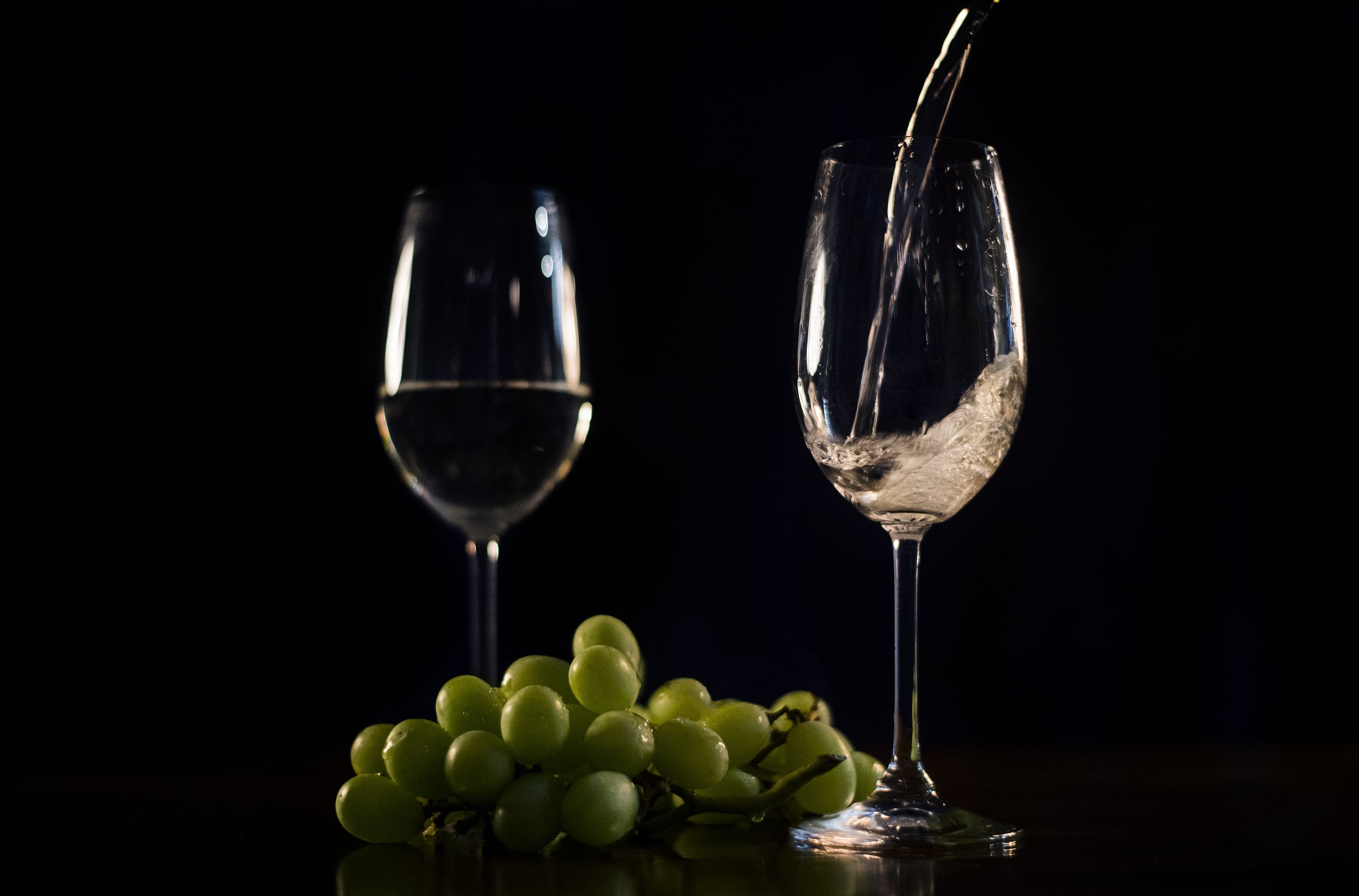 White wine being poured into a glass with grapes on surface next to it